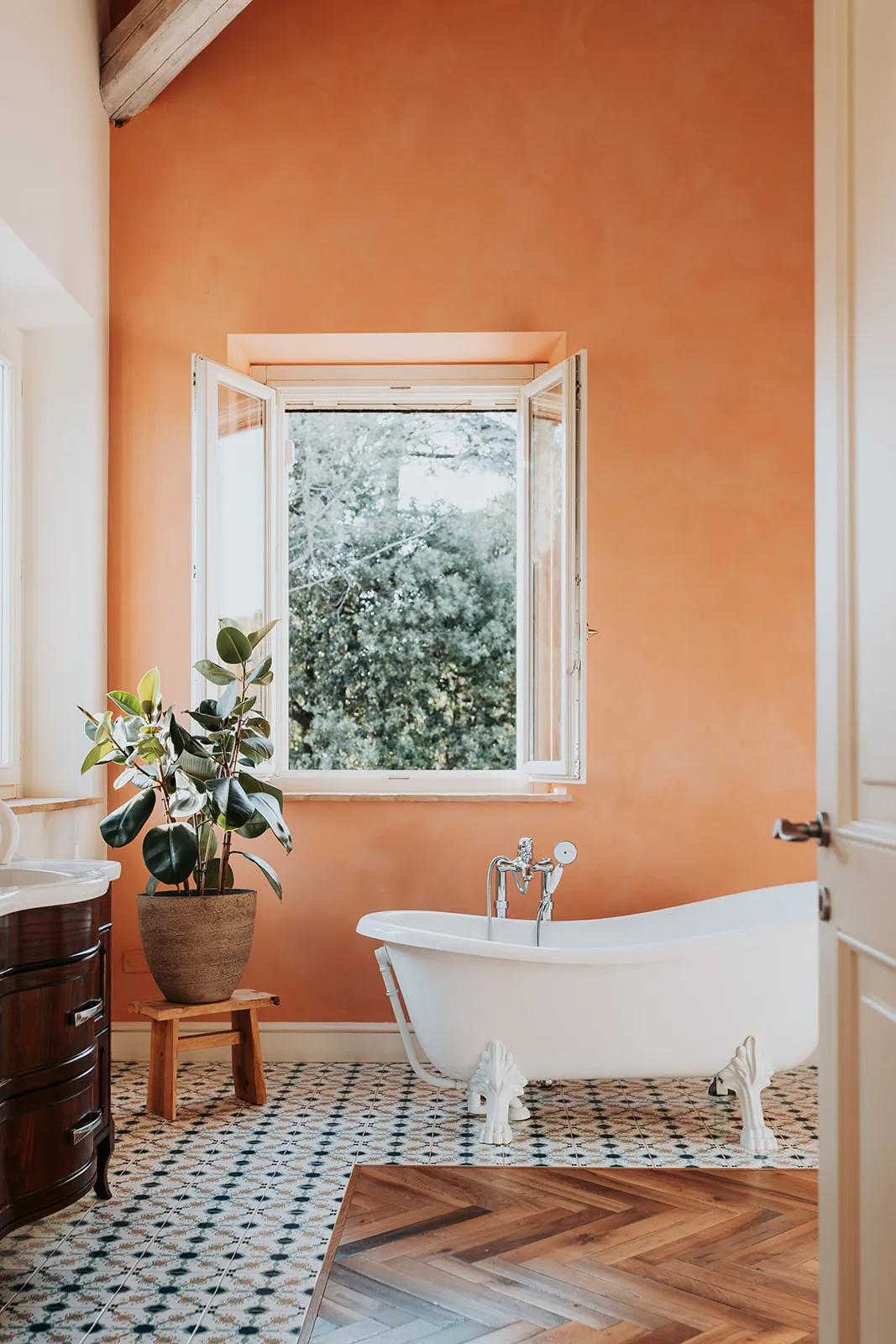 Badezimmer mit Klauenfußwanne, Terrakotta-Wand und einem Fenster mit Blick in die Bäume
