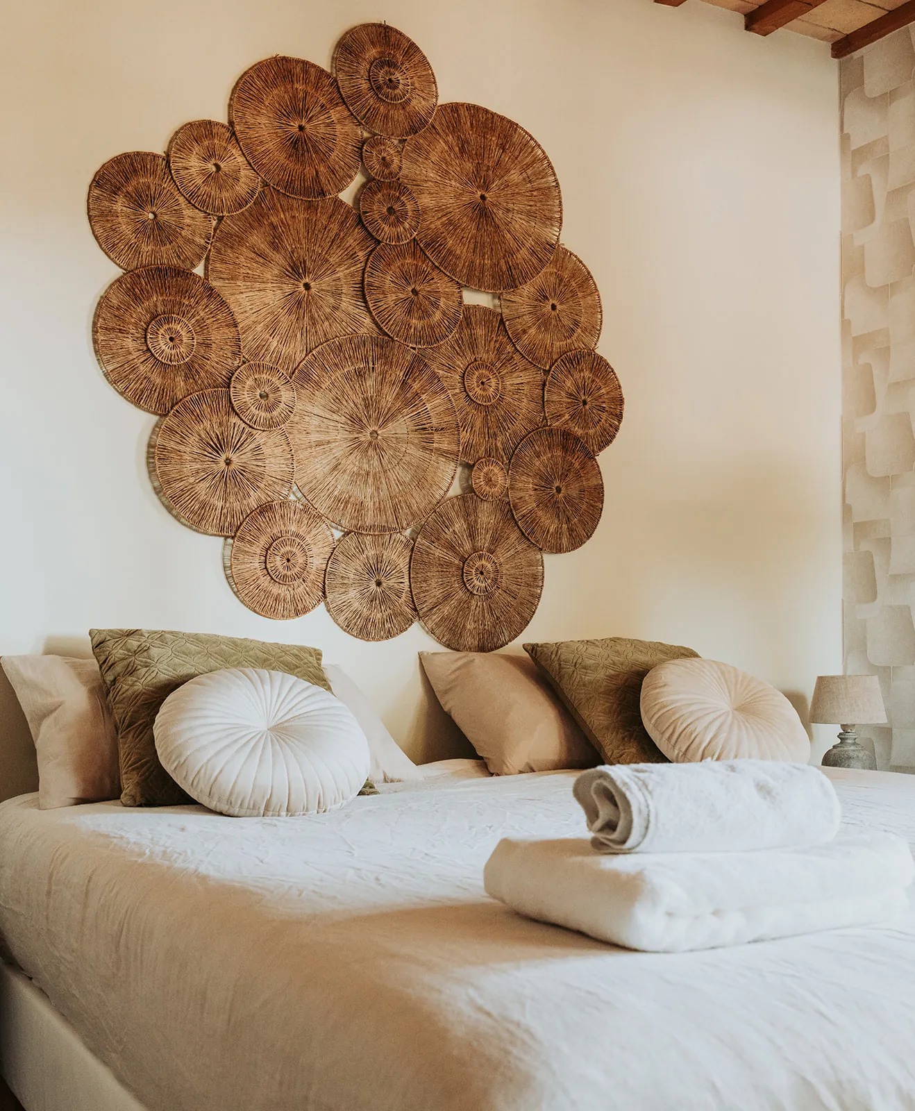 Schlafzimmer mit gewebtem Wandkunstwerk, Leinenbettwäsche und gefalteten Handtüchern