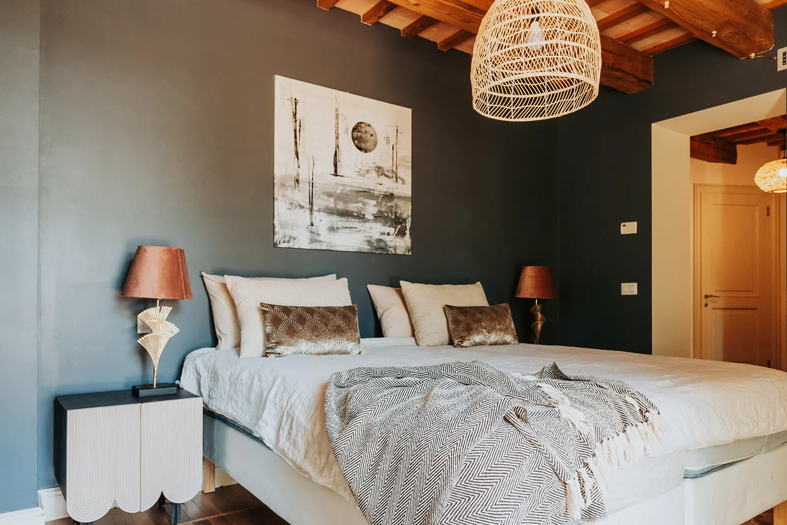 Schlafzimmer mit dunkler Wand, Rattan-Pendelleuchte und Messinglampen