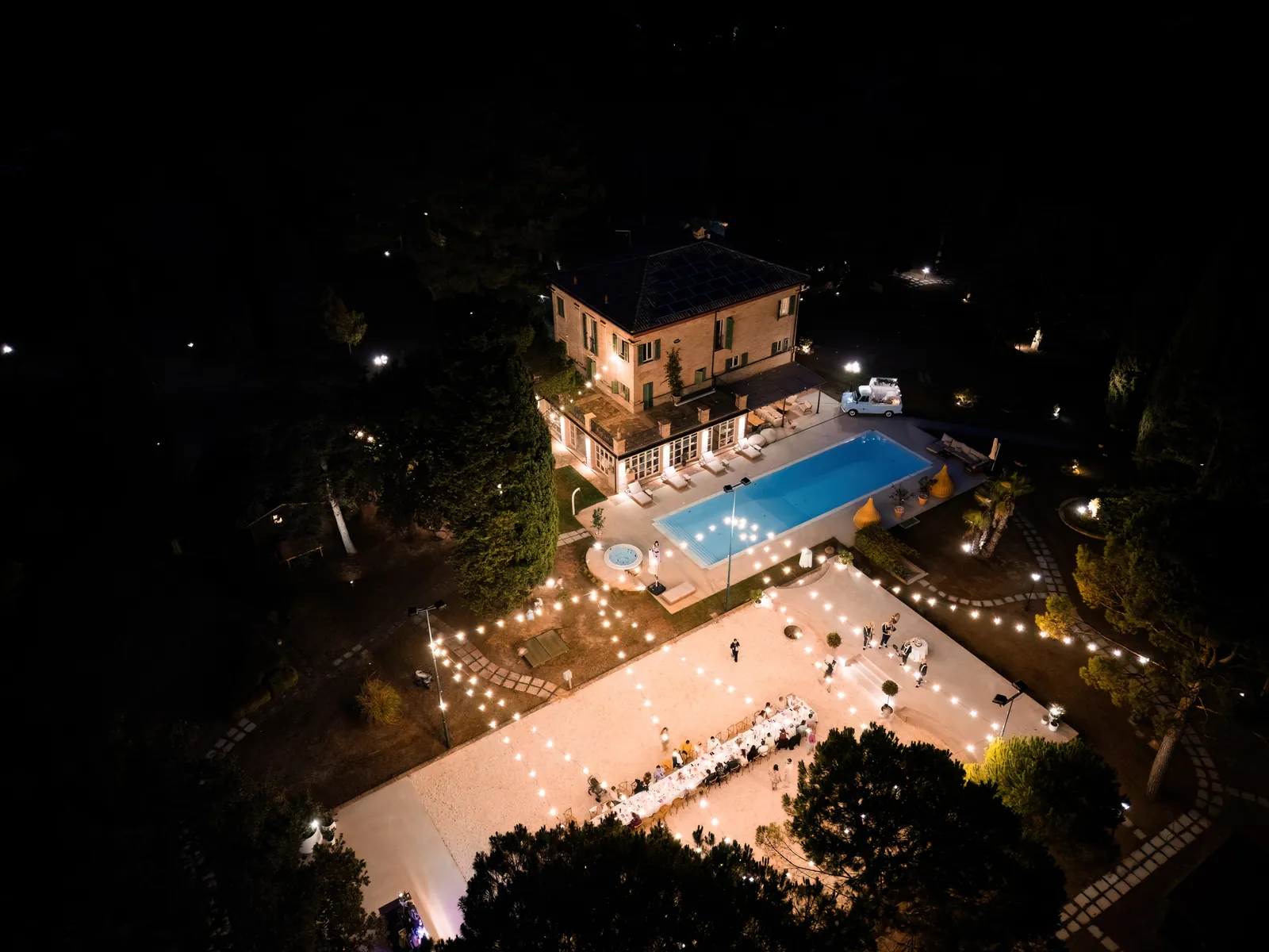 Night drone view of the lit villa, pool and party