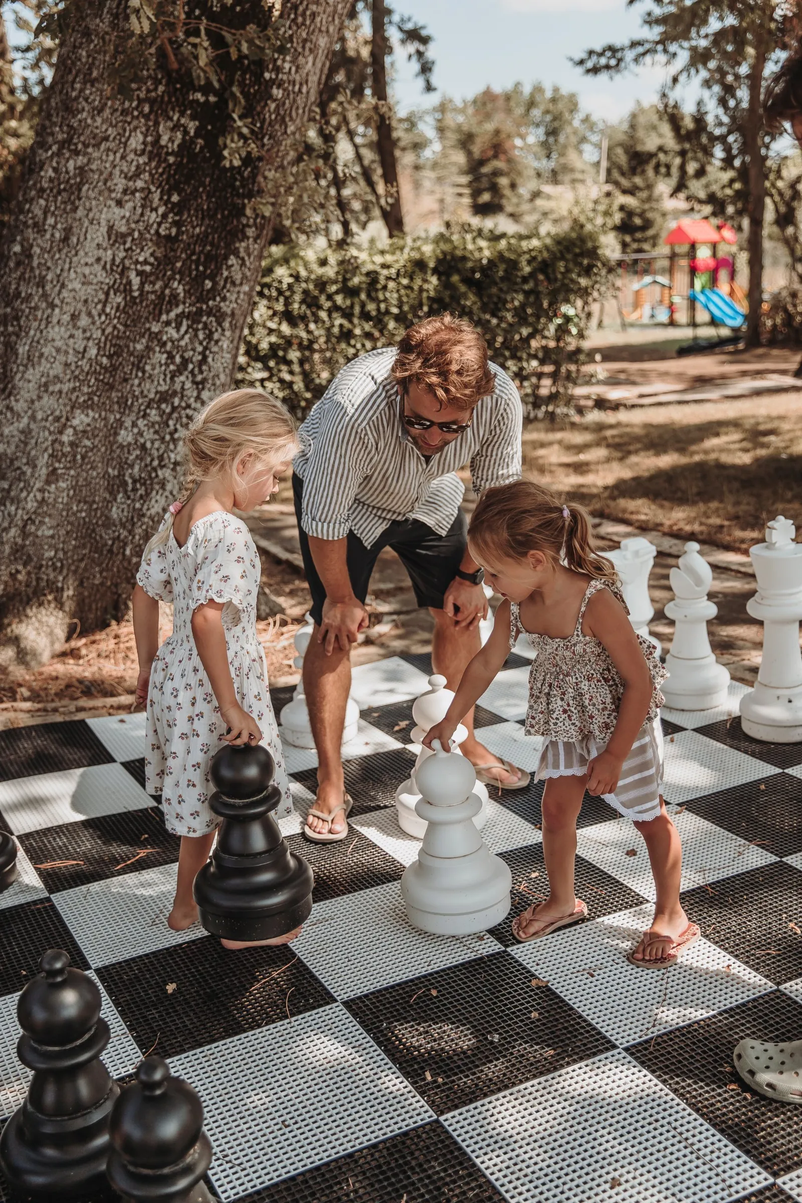 Kinder spielen Riesenschach im Park, dahinter der Spielplatz