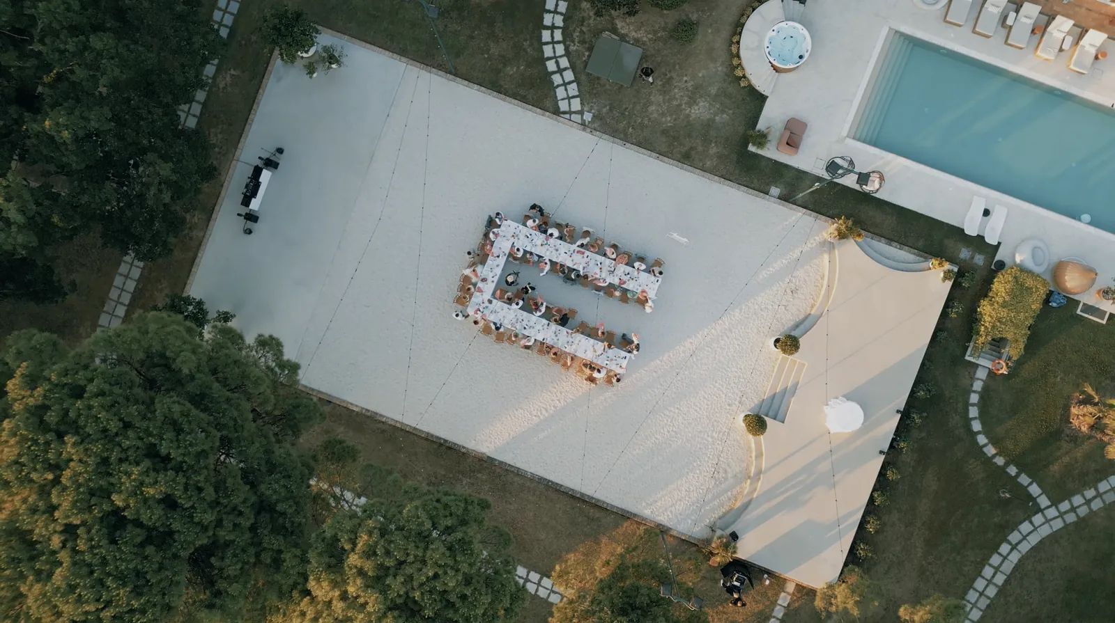 Drohnenaufnahme von oben: eine U-förmige Hochzeitstafel im Bühne & Dinner-Bereich neben dem Pool
