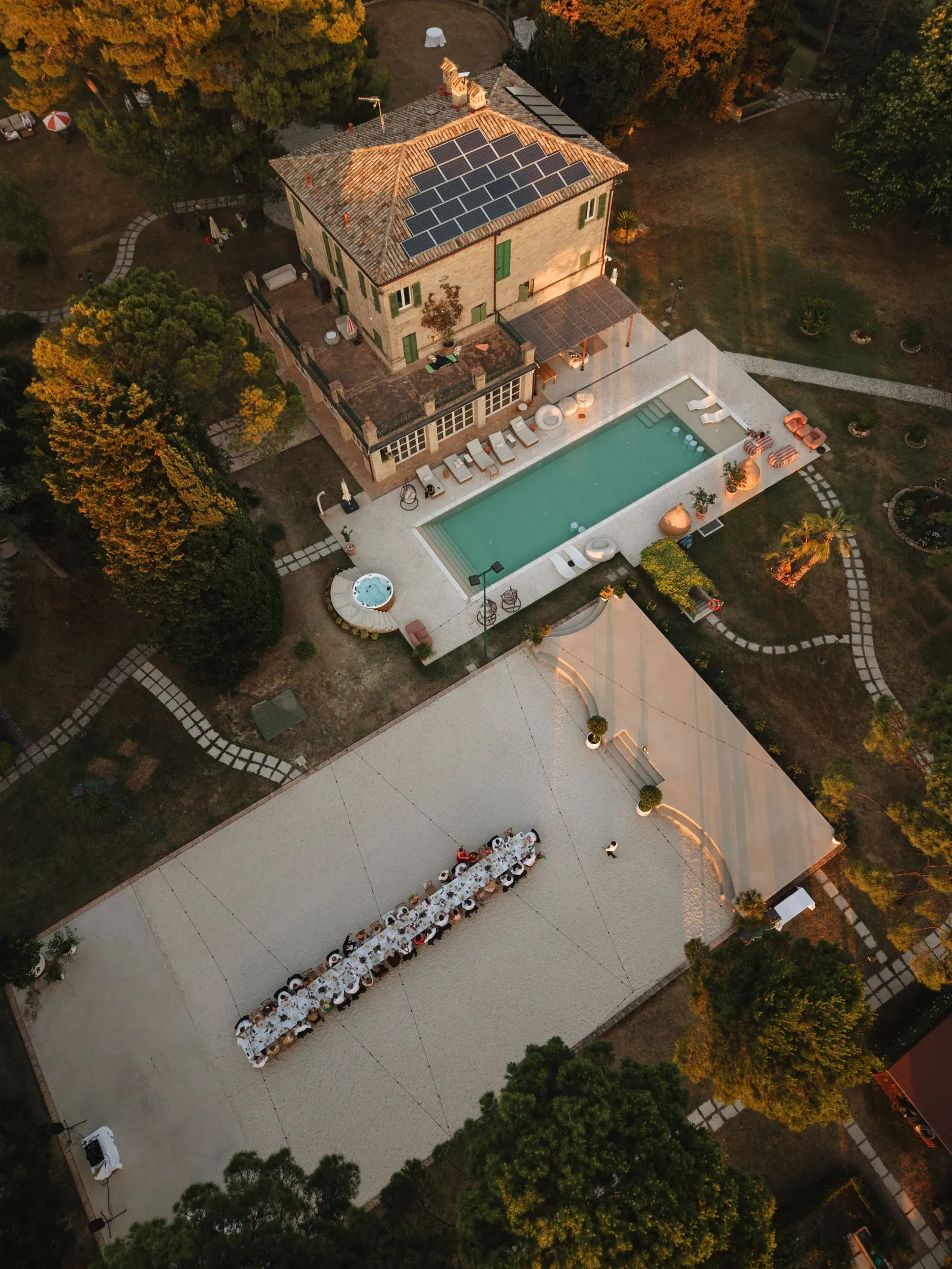 Drohnenaufnahme von oben auf die Villa, den Pool und eine lange Tafel