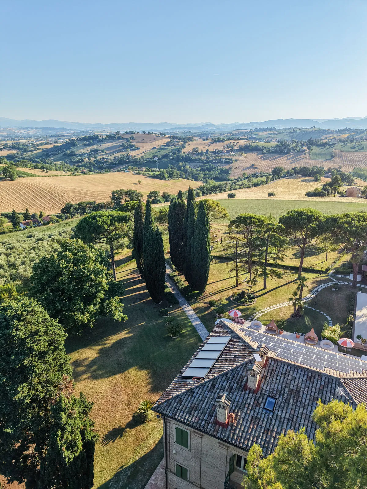 Drone view over the villa roof, the cypress lane and the rolling hills of Le Marche