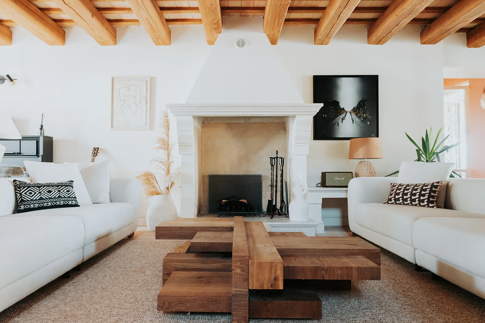 Wohnzimmer mit Steinkamin, zwei weißen Sofas und einem skulpturalen Couchtisch aus Eiche