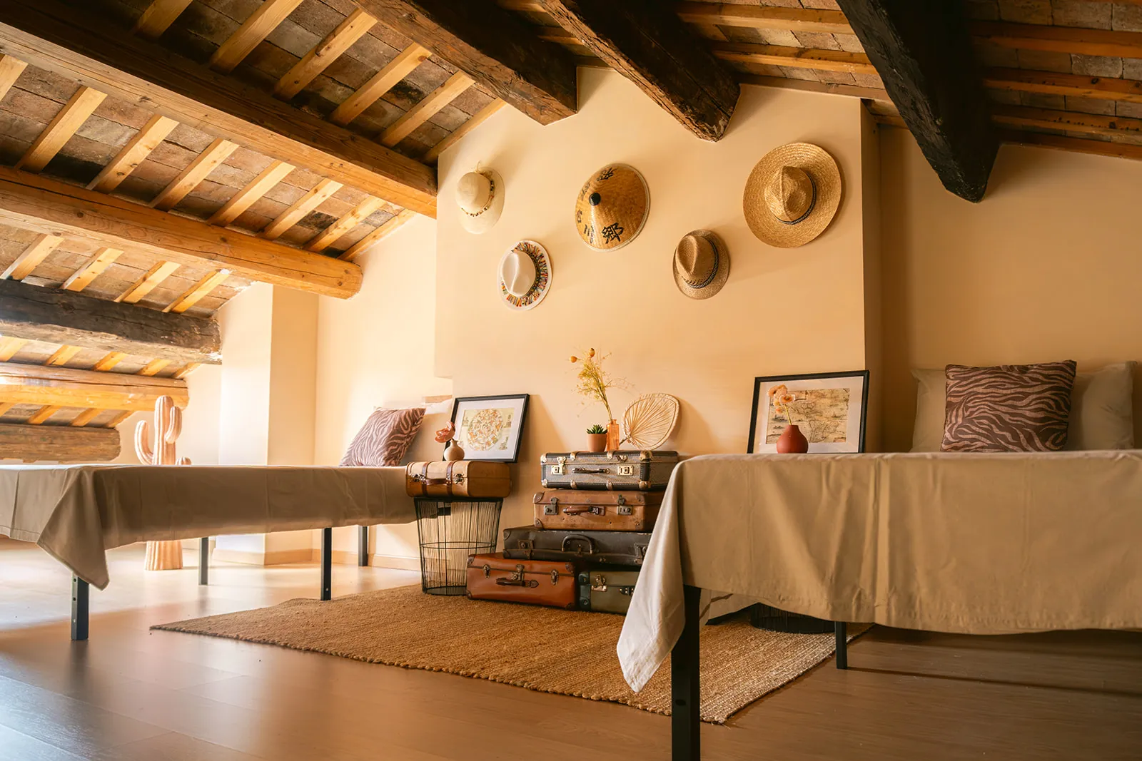 The Honeymoon: ein Dachschlafzimmer unter alten Balken, mit Strohhüten aus aller Welt und gestapelten Vintage-Koffern