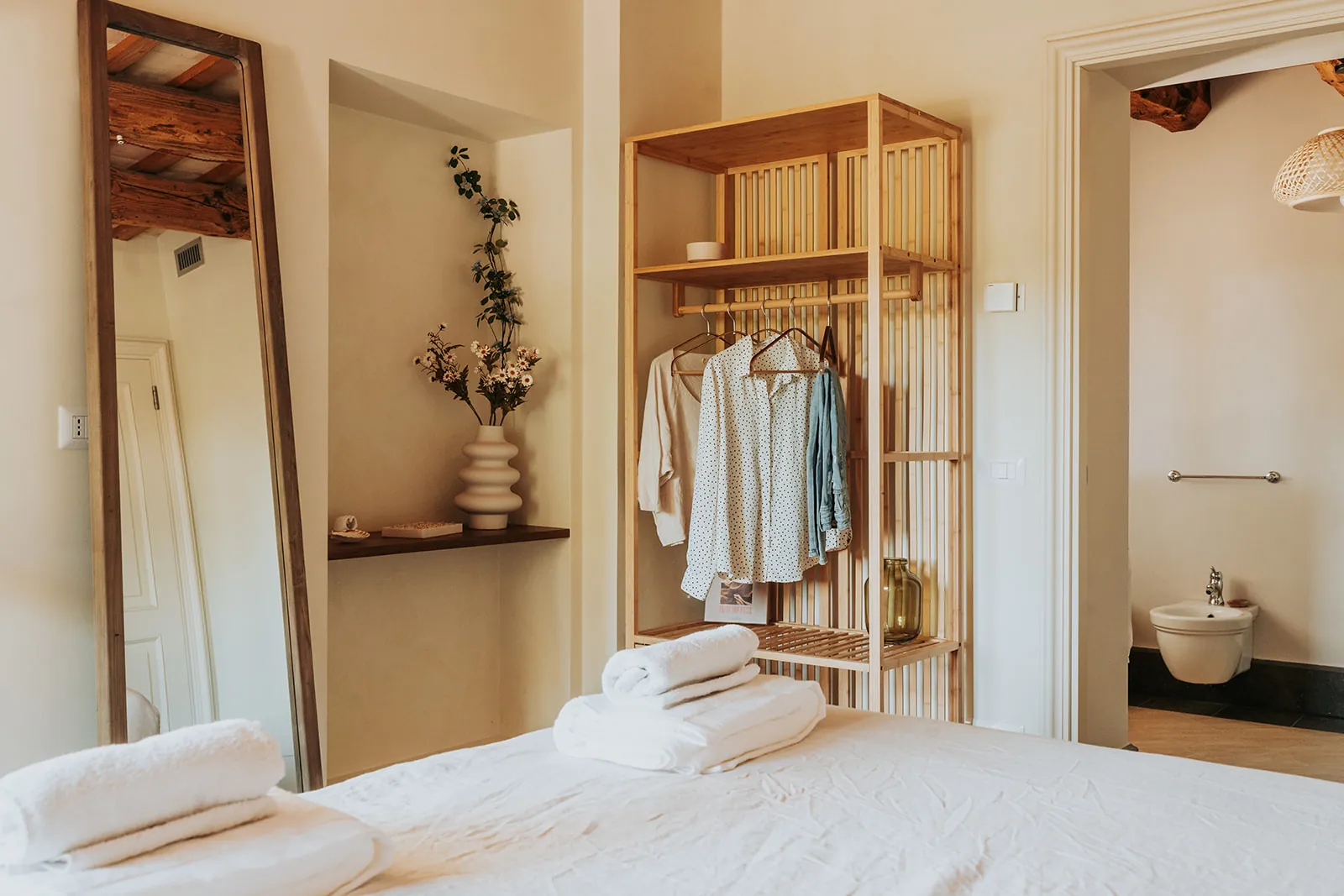 Ein hoher Spiegel, Blumen und ein offener Kleiderschrank in The Rings, dahinter das Bad
