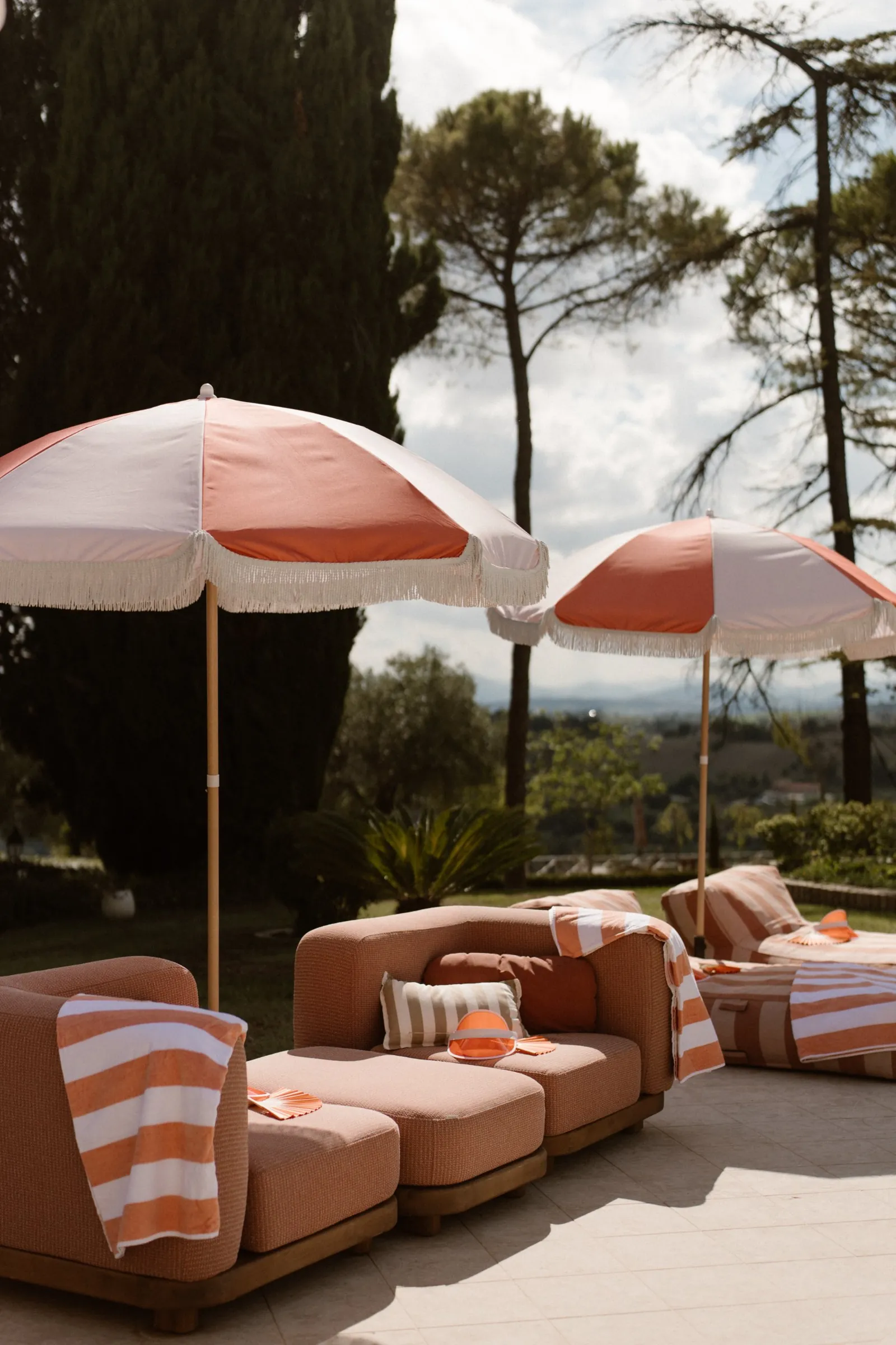 Lounge am Pool mit rosa Fransenschirmen und gestreiften Handtüchern