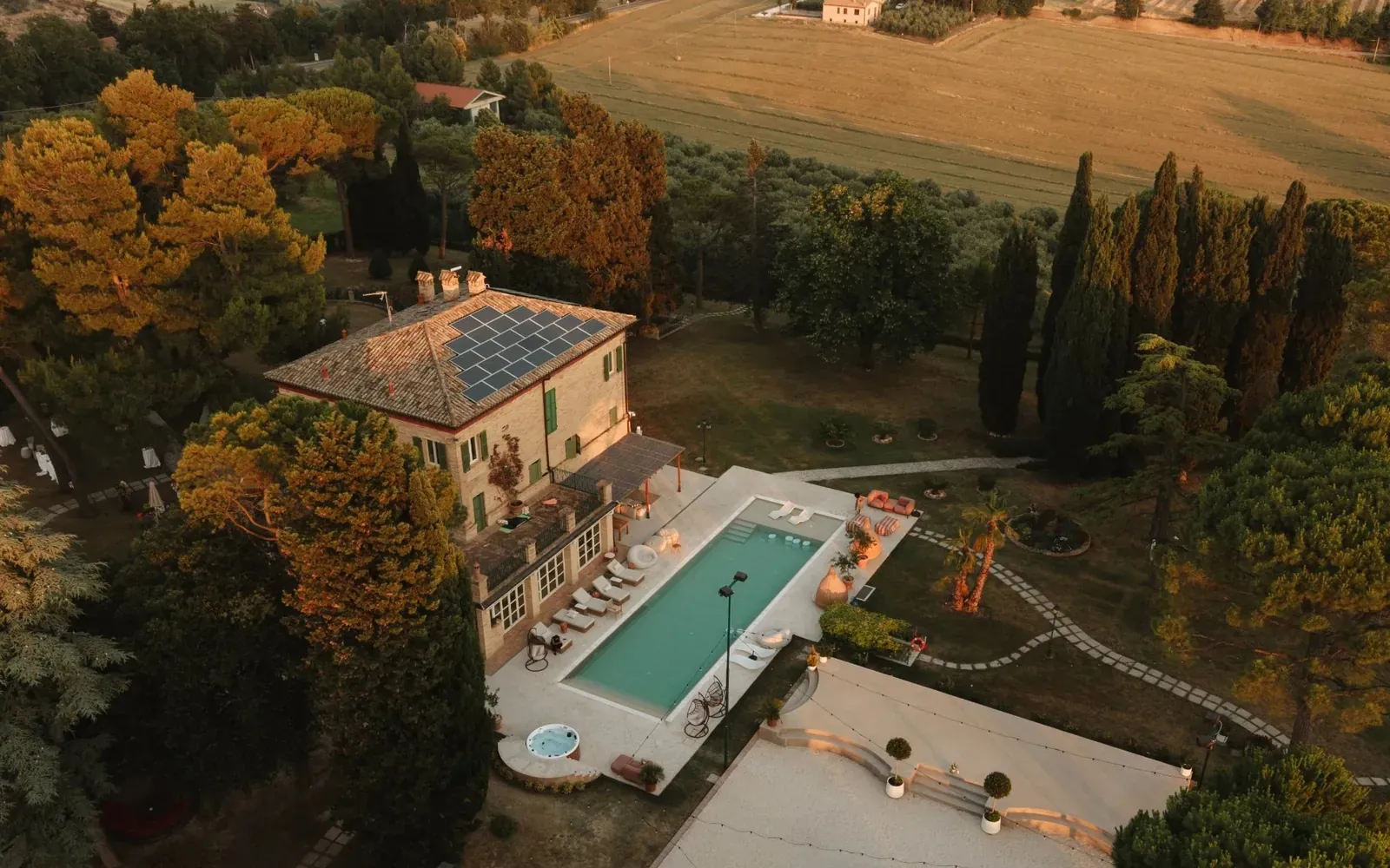 Die Villa und der Pool von oben zur goldenen Stunde, dahinter die Hügel der Marken