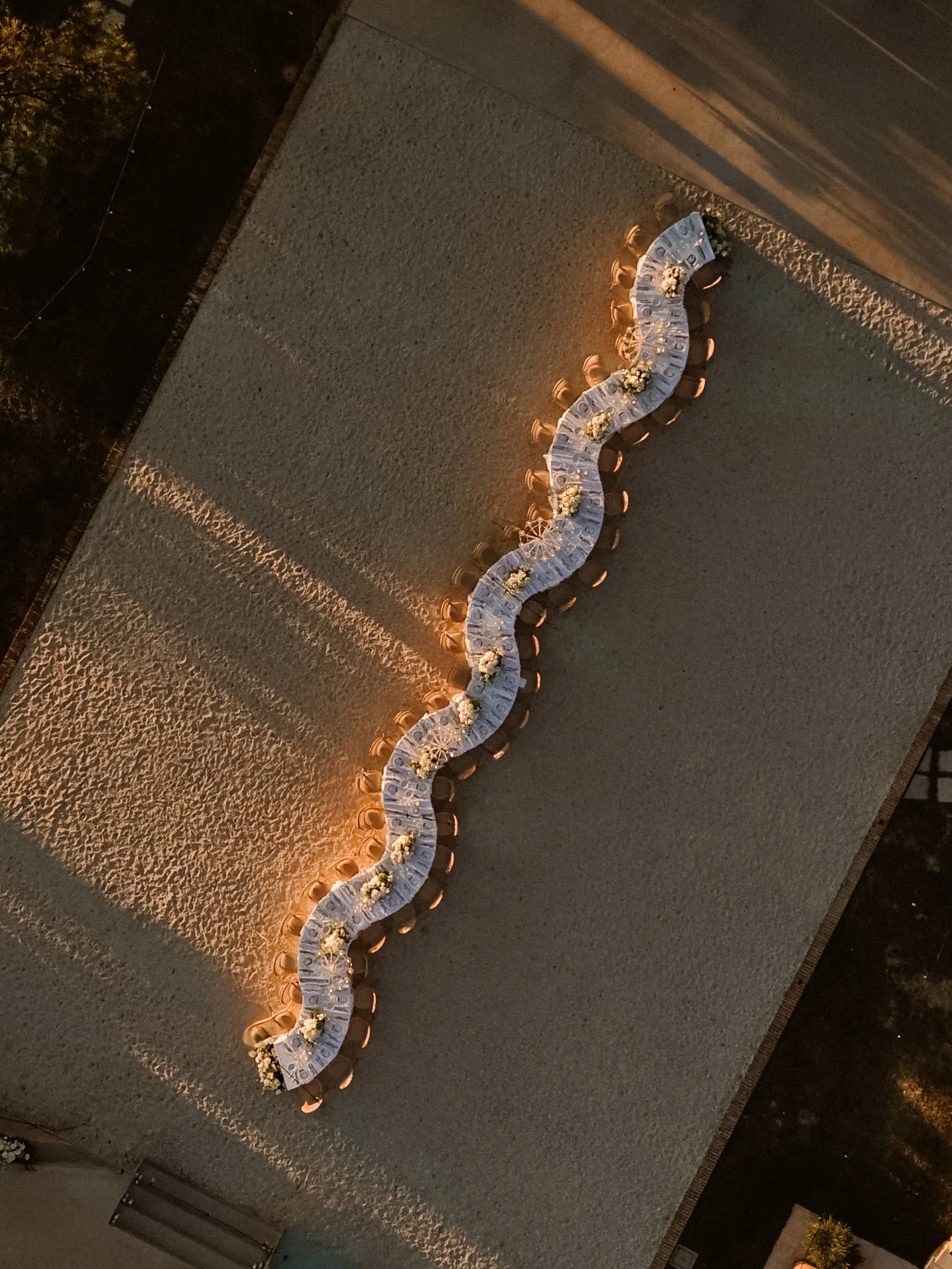 Drohnenblick auf eine geschwungene Hochzeitstafel zur goldenen Stunde