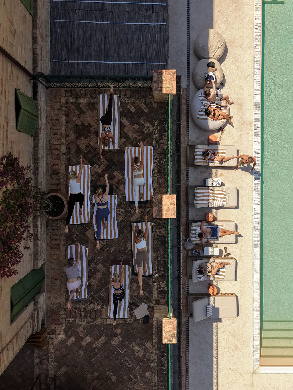 Drohnenblick auf eine Yogastunde auf der Terrasse am Pool von Maniero, Gäste entspannen auf den Liegen